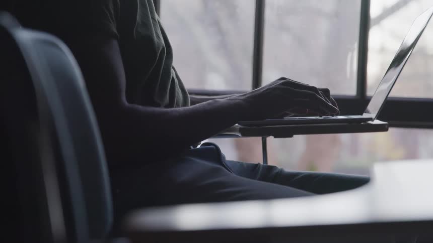 A man sitting in a chair typing on a laptop on a desk