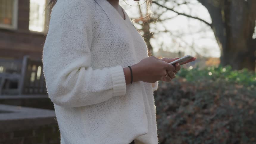 A young woman stands outdoors as she holds her smart phone