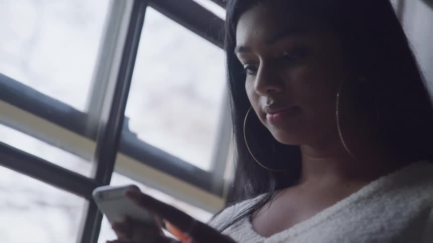 Woman wearing big earrings uses a smartphone near a window