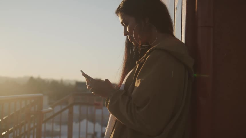 A teenage girl standing outside her house uses her cell phone