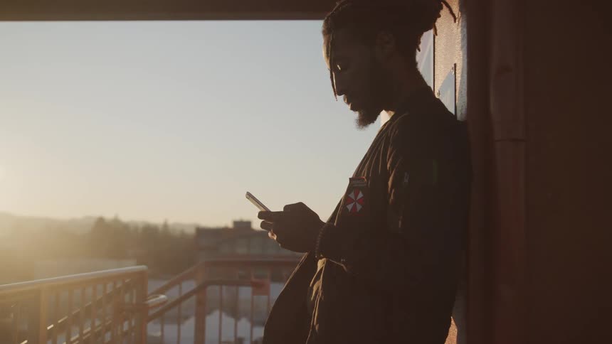 A man stands on a balcony looking at his cell phone