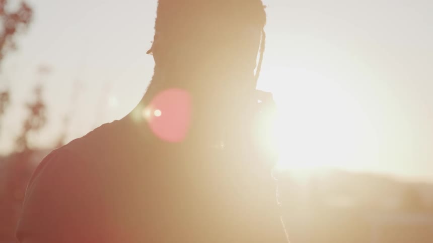 Man is silhouetted by suns glare as he talks on mobile phone outdoors