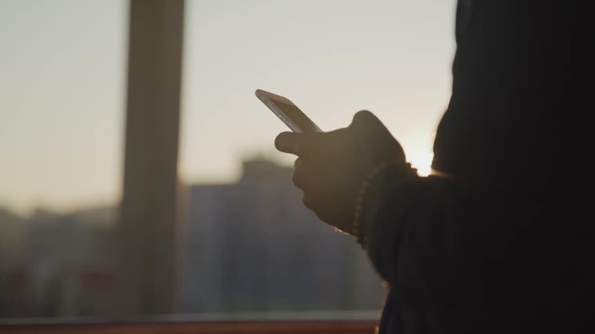 Person texting on cell phone in front of setting sun