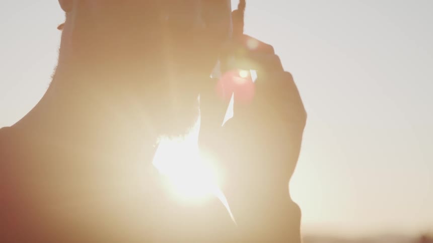 A man talks outside on his smartphone as bright sunlight shines down on him