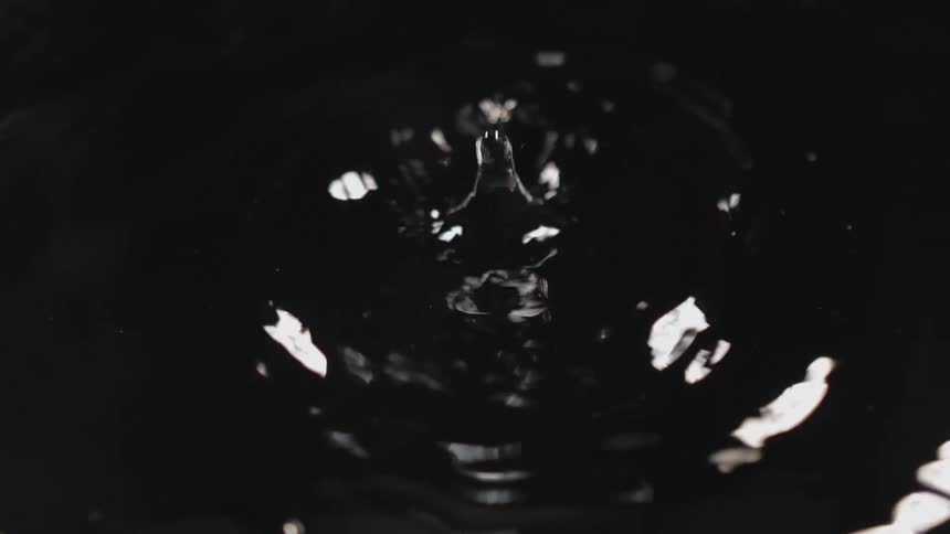 Water droplets falling into water with ripples and light reflecting off the water