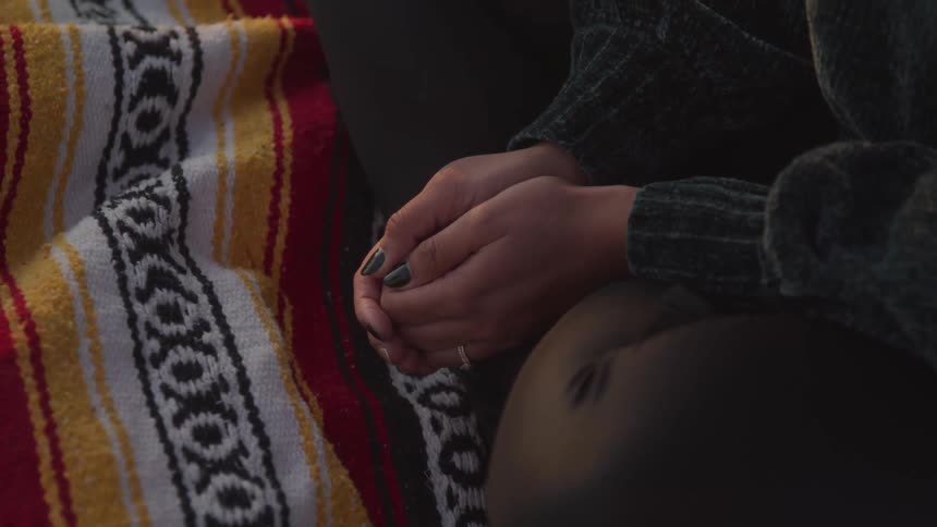 Person sitting cross legged on blanket with hands held together