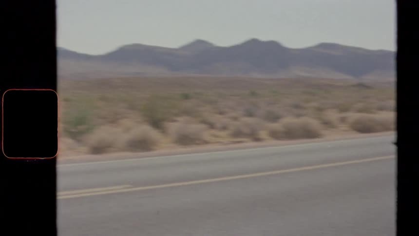 A motorcyclist rides down a road through a shrubland during the day