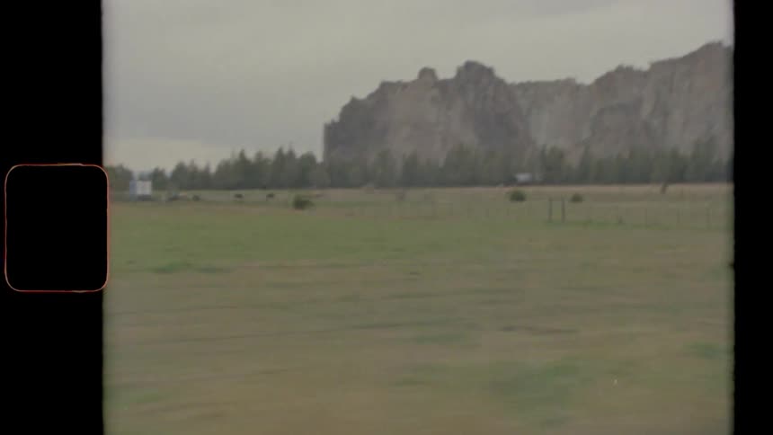A grassy plain with trees a cliff the sky and clouds in the background