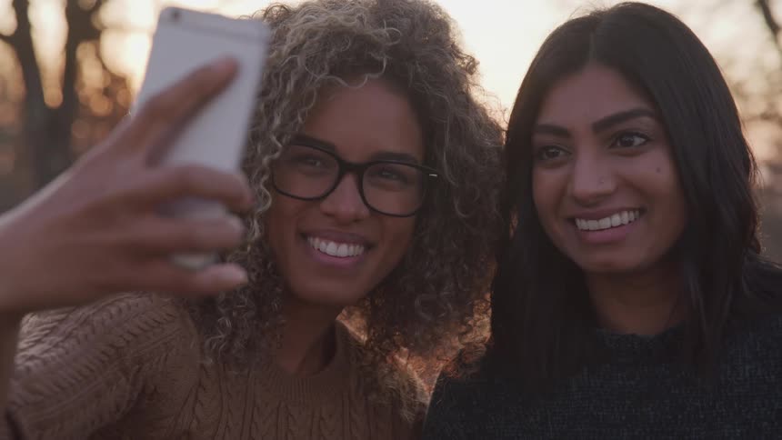 Two teenage girls pose as they take a selfie with a cell phone