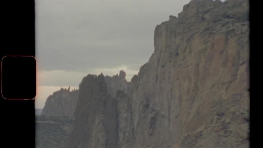 Under a cloudy sky a large rock formation has very steep sheer cliff sides