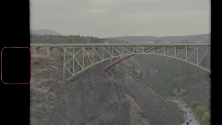 Vintage footage of cars driving across a bridge over a river