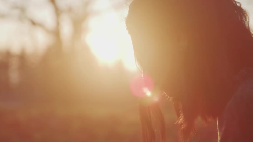 The sun shines down on a teenage girl sitting outside looking at the ground