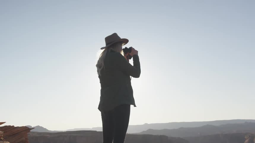 A person with a hat standing looking through binoculars with the sky in the background