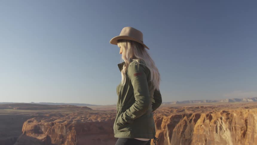 A young woman stands and looks over a cliff