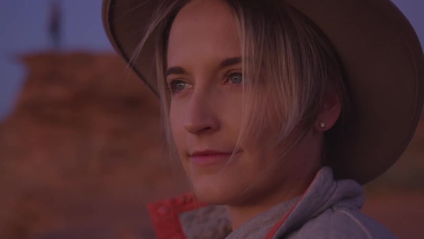 A woman is standing outdoors while wearing a hat at dusk