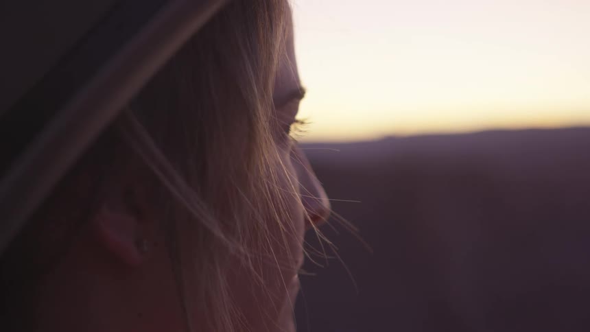 Young woman in hat looks towards horizon at sunset