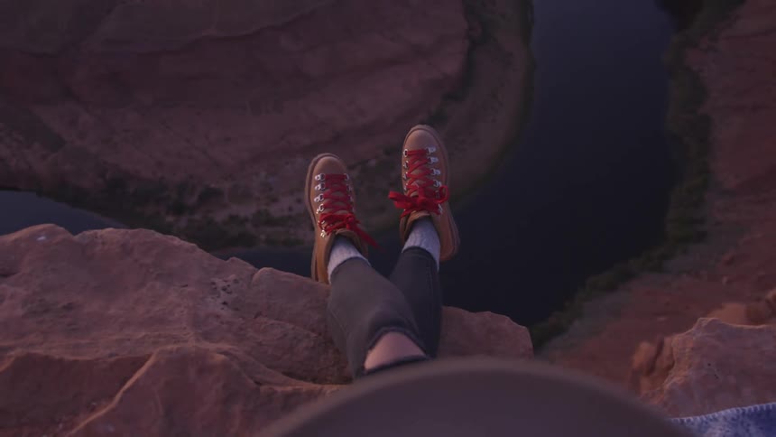 Woman sits near edge of cliff overlooking river bend