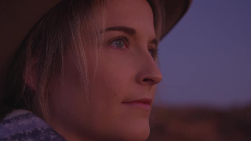 A young blonde haired woman looks off into the distance while outdoors