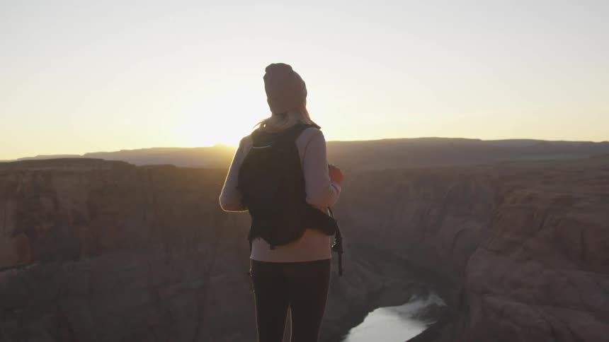 A woman is standing on the cliff at sunrise