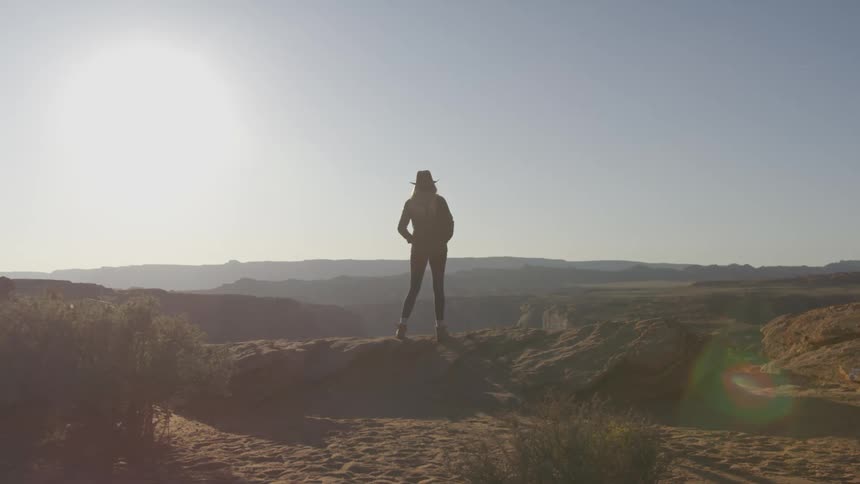 A woman with a hat standing near a cliff with a canyon the sky and clouds in the background