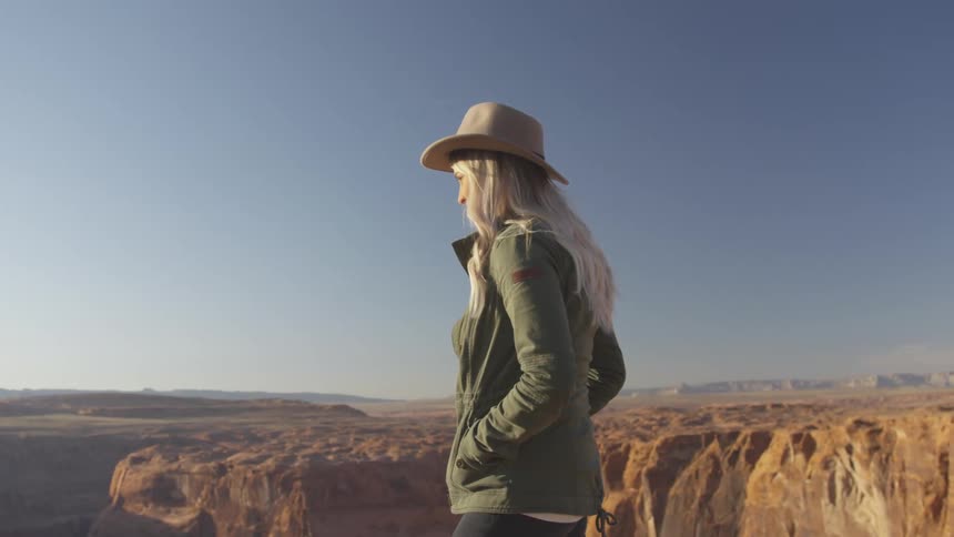 A woman is wearing a hat outdoors by a landscape