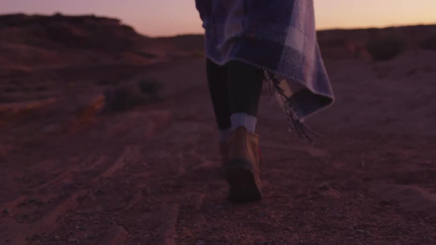 A female walks through a desert area as the sun sets