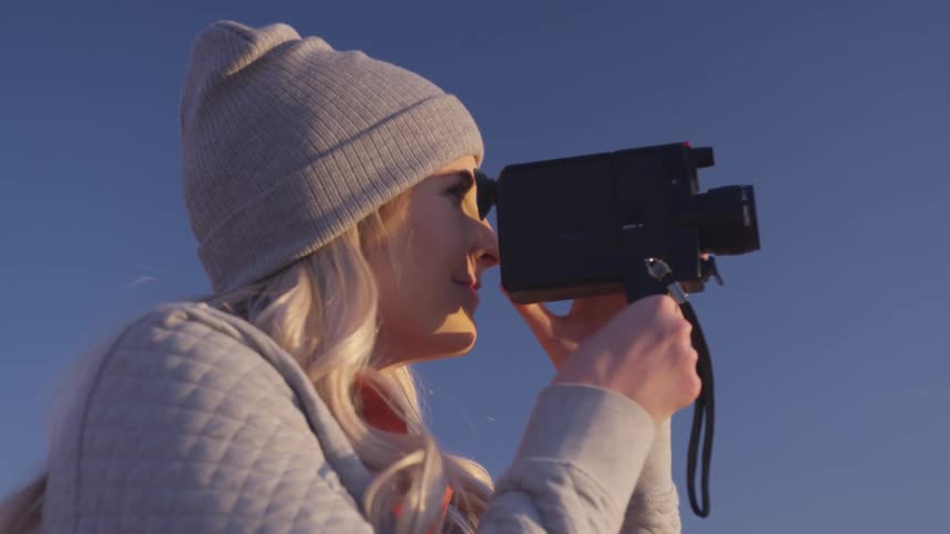 A woman standing outside films with a vintage recorder