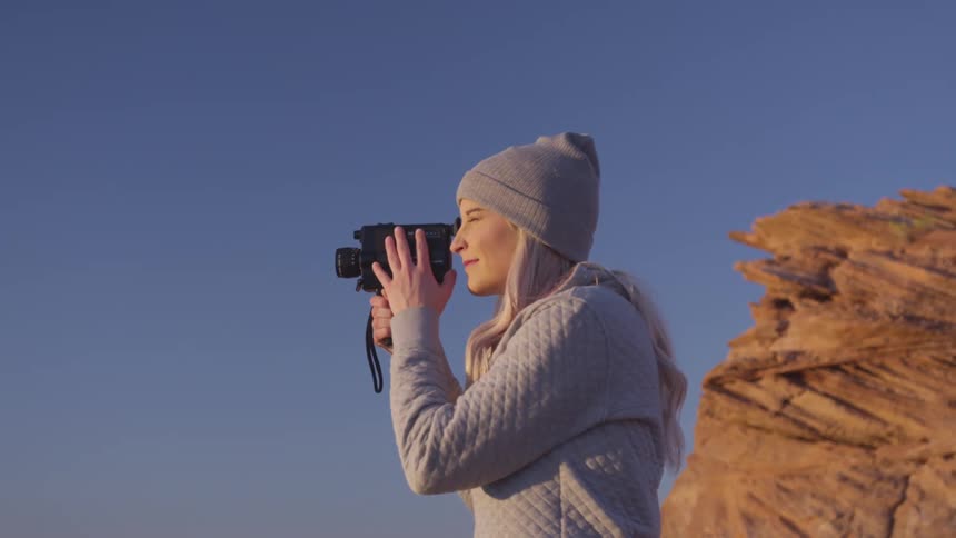 Young blonde woman holds a video camera filming on the desert