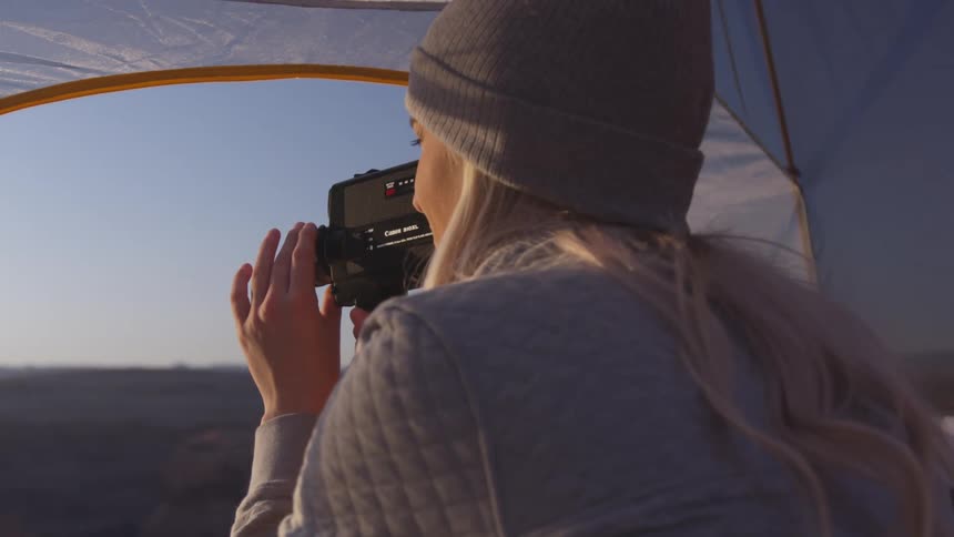 Woman sitting in tent films landscape with camcorder