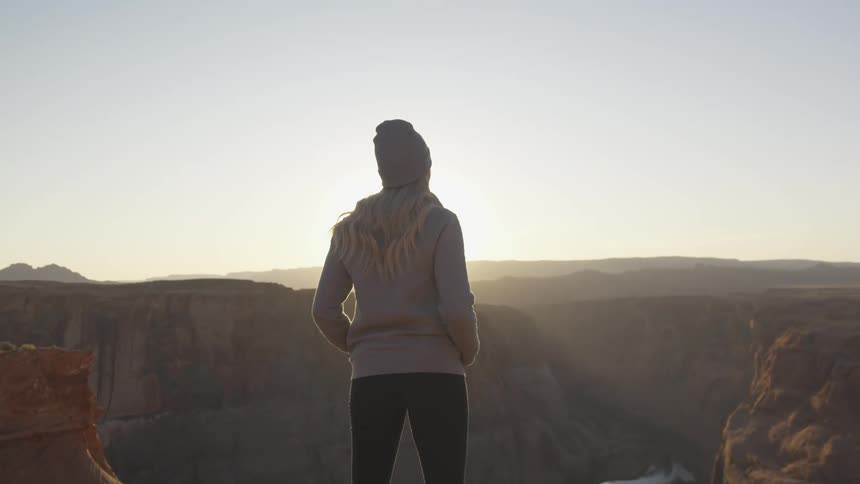 A woman stands above a canyon on mountain looking to the scenery