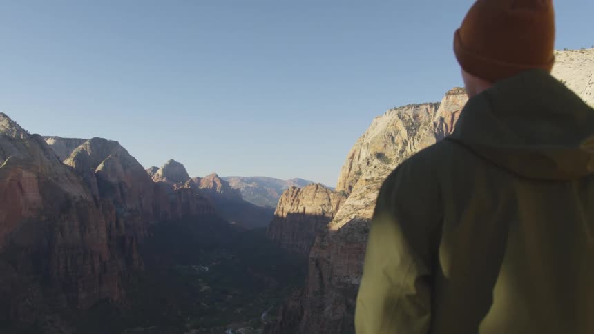 A young man stands on top of a canyon and looks at the landscape of canyons and the valley