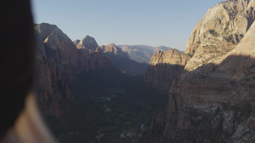 A woman standing on top of a cliff looks at the canyons and the valley below her