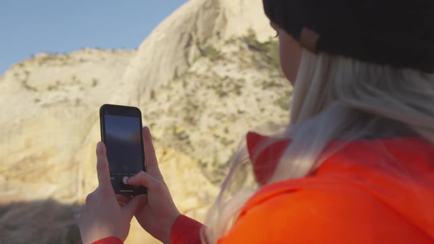 A young woman takes pictures of a canyon on her phone