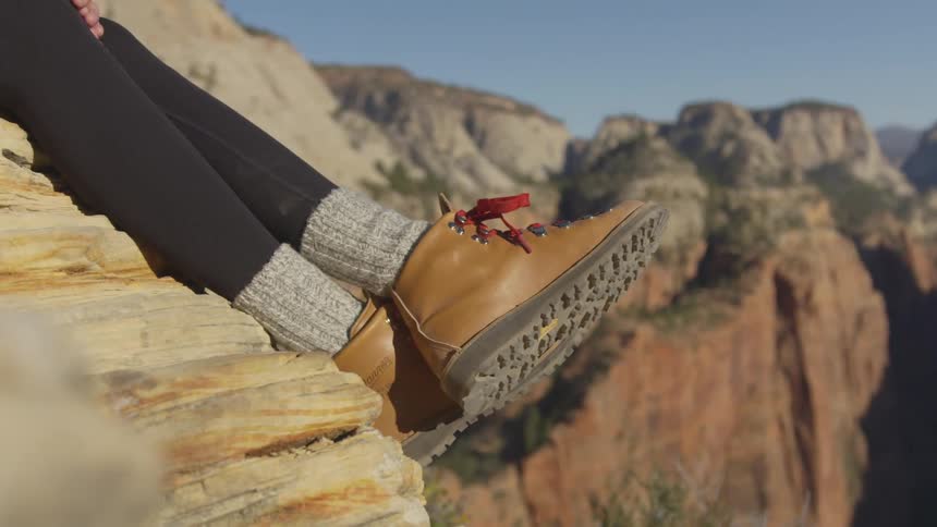 Close up of the shoes of a woman sitting in the ledge of a cliff in the mountains