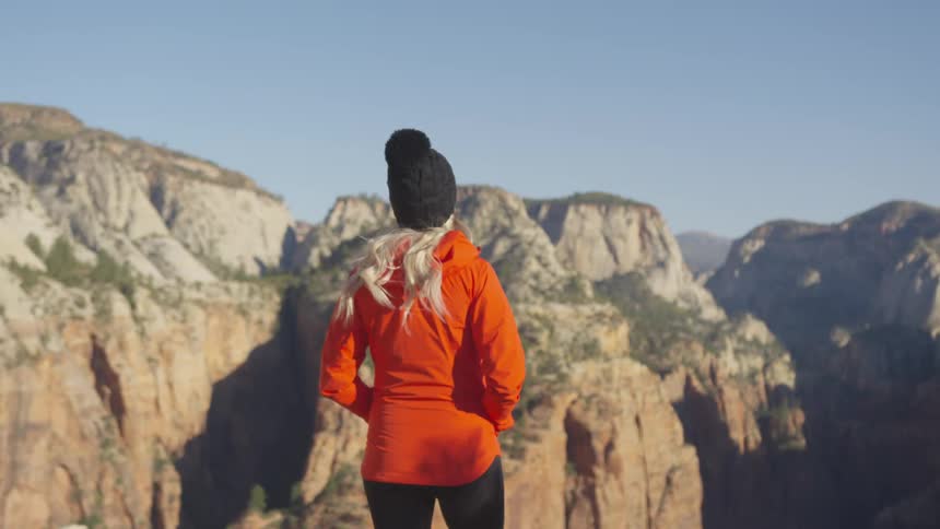 A woman standing on a cliff looks at the canyons across from her