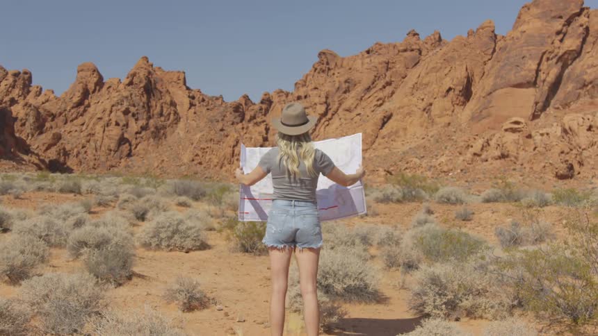 A woman holds a large map up while standing in a dry desert terrain
