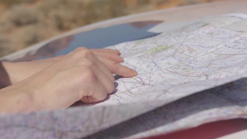 Wind blows up a paper map placed against a vehicle windshield by a woman on a road trip