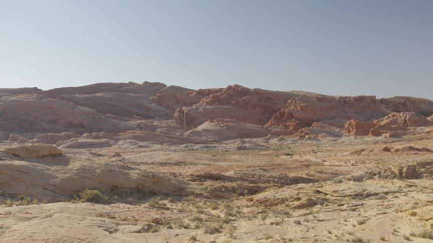 Arid terrain leads to rough vegetation free mountains under clear blue sky