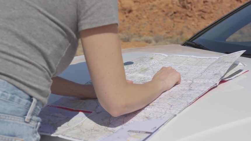 Woman leans over map on hood of car tracing route