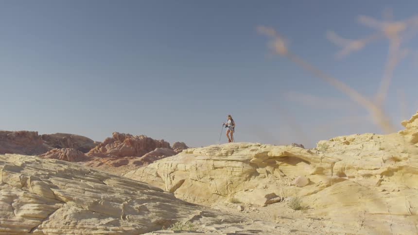 A woman uses two walking sticks as she walks the summit in a canyon
