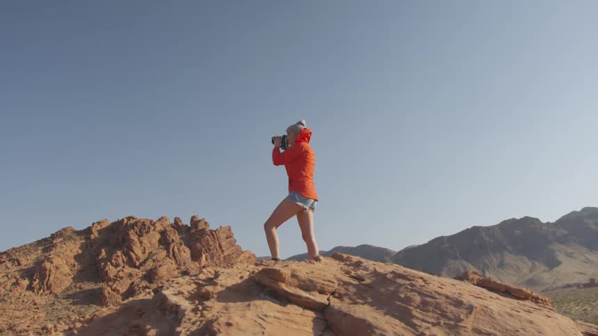 A young woman standing on a canyon takes pictures with her camera
