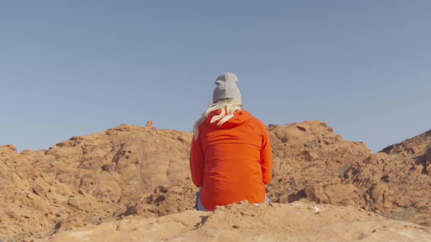 A woman is sitting by a rock formation outdoors