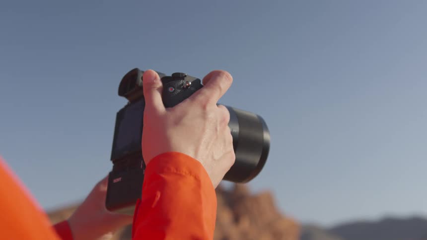 Young blonde woman wearing red jacket takes pictures of the desert with a camera