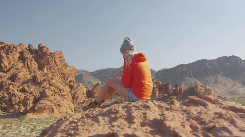 A woman sits on a rocky dry desert terrain quietly