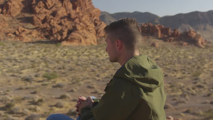 A man sitting on a stone in the badlands with his head bowed in contemplation slowly raises his head
