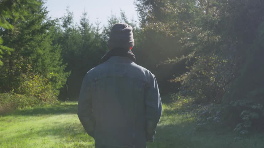 Man with a grey beanie and a coat walks on a trail in the forest