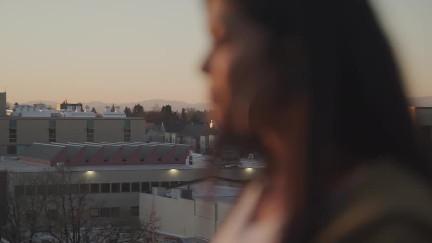 Side view of a woman standing on a top of building in blurry vision with buildings in the background