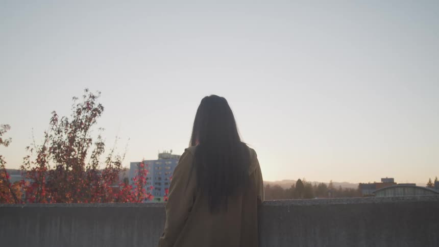 A woman stands on a city building balcony looking to the distant scenery