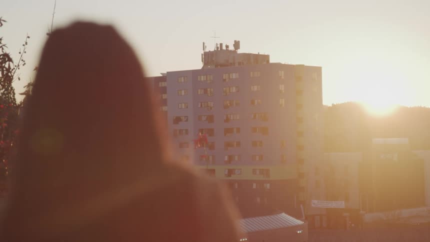 Light from sun sitting at horizon behind building turns woman into silhouette briefly
