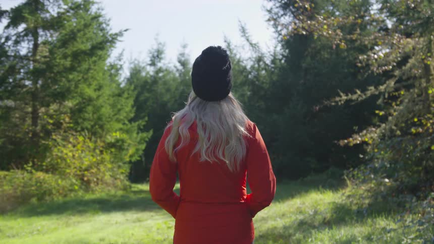 Young woman walks on grassy path through forest